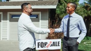 Realtor and buyer shaking hands in front of a SOLD sign